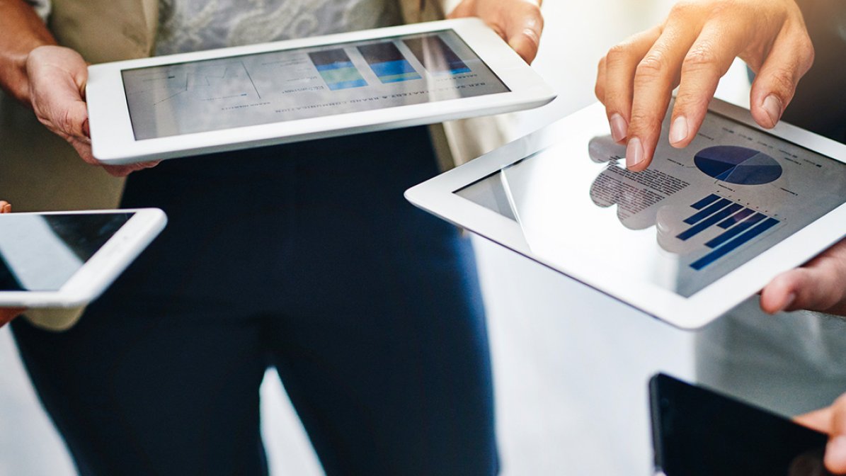 People gathered reviewing charts and data on tablet devices