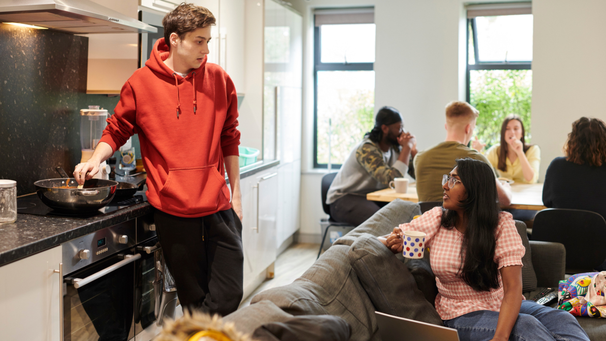 A group of students gathered in a communal living area, cooking and talking. 
